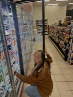 a woman is sitting on the floor in front of a grocery store shelf and reaching up to grab something