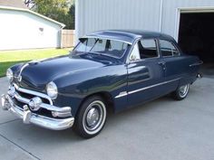 an old blue car parked in front of a garage