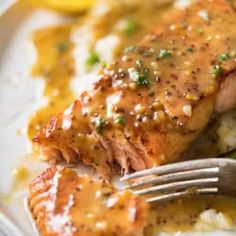 a piece of salmon covered in gravy on top of mashed potatoes