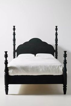 a black bed frame with white sheets and pillows on the headboard, in front of a white wall