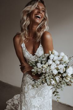 a woman in a wedding dress holding a bouquet of flowers and smiling at the camera