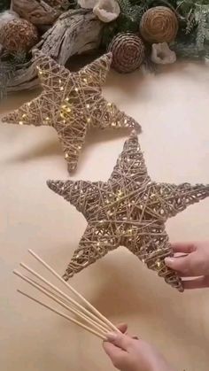 someone is holding two star shaped candles in front of some christmas tree branches and decorations