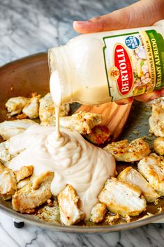 someone pouring dressing onto chicken in a skillet