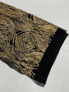 a black and gold scarf with sequins on the edges is laying on a white surface