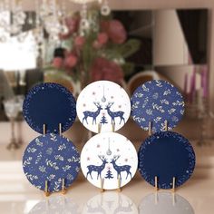 four paper plates decorated with blue and white deer designs, on a table in front of a mirror