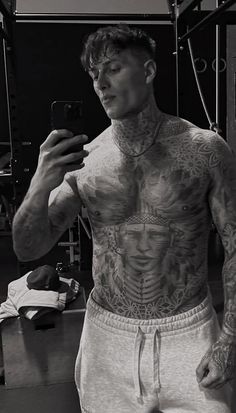 a man with tattoos taking a selfie in front of a mirror while holding a cell phone