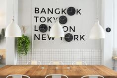 a wooden table topped with white chairs next to a wall mounted clock on the wall