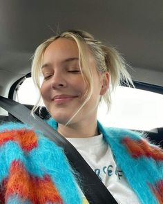 a woman sitting in the back seat of a car wearing a fuzzy blue and orange coat