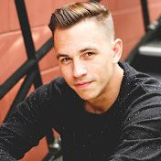 a man with a pomp undercut sitting in front of a wall and looking at the camera