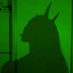 the shadow of a man's head on a green wall in a dark room