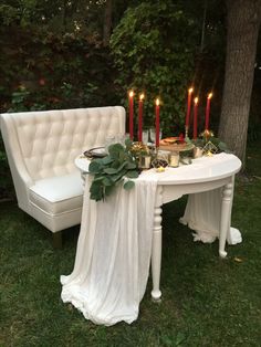 a white table with candles on it in the grass next to a couch and chair