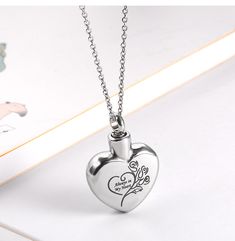 a silver heart shaped pendant with an engraved message on the front and back, sitting on a white surface