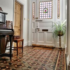 a room with a piano, potted plant and stained glass window on the door