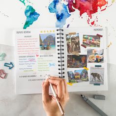 a person holding a pen and looking at an open travel book with pictures on it