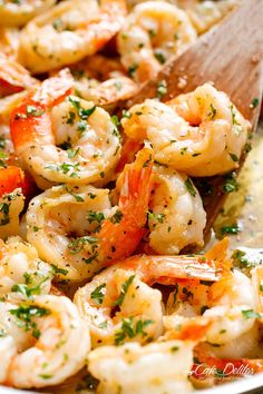 shrimp and carrots being cooked in a skillet with a wooden spoon