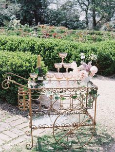 a table with wine glasses and flowers on it in the middle of a garden area