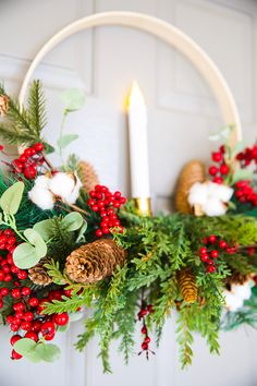 a wreath with pine cones, berries and greenery is hung on the door by a candle