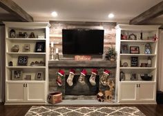 a living room with christmas stockings hanging on the fireplace mantel and shelves filled with holiday decorations