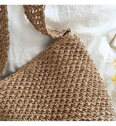 a straw bag sitting on top of a bed next to a pillow and yellow flowers