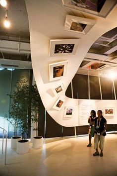 two people standing in front of a wall with pictures on it and hanging from the ceiling