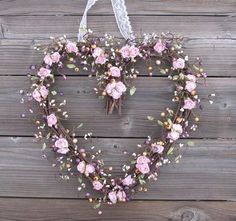 a heart shaped wreath with pink flowers hanging on a wooden wall in the shape of a heart