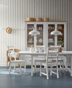 a dining room table with chairs and two lamps on the wall above it, in front of a striped wallpapered wall