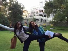 two young women are posing for the camera in front of a large building and trees