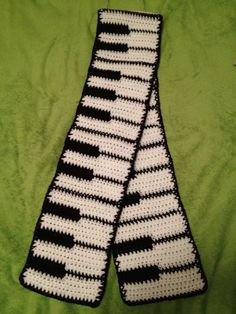 two crocheted black and white scarfs laying on a green cloth covered bed