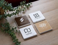 four square coasters sitting on top of a wooden table next to a potted plant