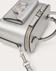 Valentino Garavani Locò mini handbag in metallic calfskin with metallic VLogo Signature detail. Can be worn over the shoulder/crossbody or carried as a handbag thanks to the handle and the adjustable and removable shoulder strap. - Palladium-finish logo and hardware - Zip closure - Nappa leather lining. Interior: one card slot - Outside pocket with magnetic closure - Adjustable and removable leather shoulder strap - Shoulder strap drop length: min 52.5 cm to max 57.5 cm / min. 20.7 in. to max. 2 Luxury Silver Shoulder Bag With Gold-tone Hardware, Luxury Silver Shoulder Bag With Detachable Handle, Silver Shoulder Bag With Top Handle And Detachable Handle, Designer Silver Shoulder Bag With Detachable Handle, Luxury Metallic Bag With Metal Hardware, Luxury Silver Satchel With Palladium Hardware, Luxury Box Bag With Silver-tone Hardware And Double Handle, Luxury Box Bag With Silver-tone Hardware, Silver Top Handle Shoulder Bag With Removable Pouch