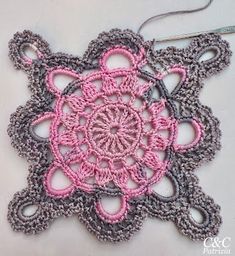 a crocheted doily with pink and gray colors on it, sitting on a white surface