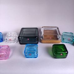 there are many different colored glass dishes on the table, each with a wooden lid