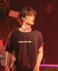 a young man standing in front of a stage with his hand on his hip while wearing a black t - shirt