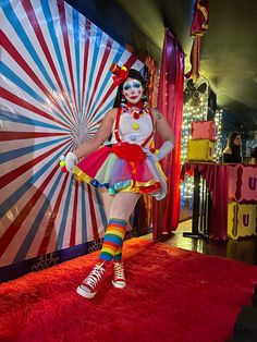 a woman dressed as a clown standing on a red carpet in front of a circus tent