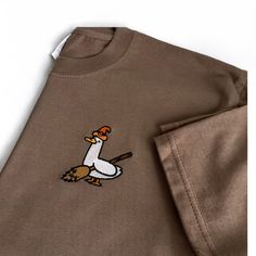 Brown organic t shirt with an embrodiered silly goose  Witchy Silly Goose T- Shirt with Halloween theme embroidery design. 👻 Unisex relaxed fit  ✨Classic silly goose dressed and ready for Haloween! Witchy goose✨ If you would like a size or colour that you can't see here then please don't hesitate to message us as we would love to try to accommodate your request as best we can 😊  ✨By buying a little something from us you will supporting a small business (entirely ran by just 2 lovely ladies ️)! Casual Embroidered Fall T-shirt, Casual Embroidered T-shirt For Fall, Fall Cotton T-shirt With Embroidered Graphics, Fall Embroidered Graphics Cotton T-shirt, Halloween Embroidered Cotton Tops, Halloween Cotton Embroidered Tops, Fall Embroidered Graphic Tee, Embroidered Graphic Tee For Fall, Embroidered Cotton Tops For Halloween