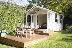 a wooden deck in front of a small white shed with chairs and table on it