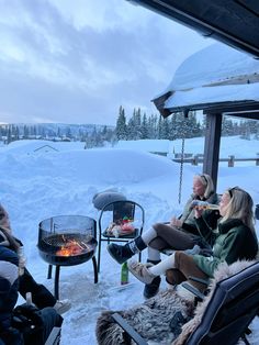 several people sitting around a fire pit in the snow with their feet up on chairs