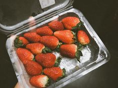 a person holding up a plastic container filled with strawberries