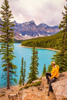 a man sitting on top of a rock next to a lake