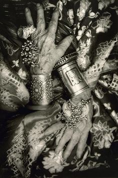 an old black and white photo of hands with bracelets on their wrists, holding cups