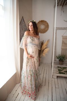 a pregnant woman wearing a floral dress standing in front of a window with her hands on her hips