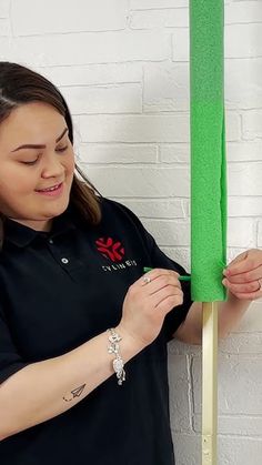 a woman in black shirt holding up a green piece of paper next to a white brick wall