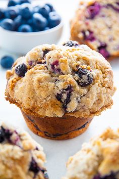 muffins with blueberries and crumbs are on a white surface next to a bowl of berries