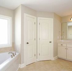 a large bathroom with two sinks and a bathtub next to a double doored window