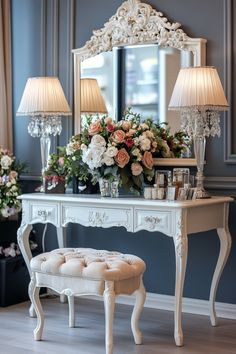 a white dressing table with flowers on it and two lamps in front of the mirror