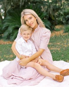 a woman sitting on top of a white blanket next to a boy in a dress