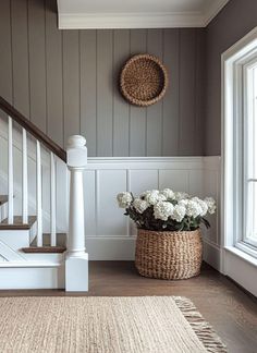 a basket with flowers sitting on the floor in front of a stair case next to a window