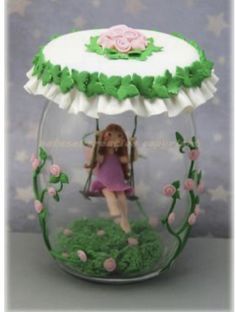 a doll in a glass jar with flowers and grass on the bottom, holding a swing