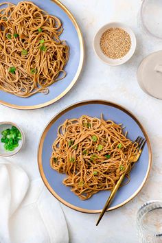 two plates of noodles with chopsticks on the side, next to bowls of rice and seasoning