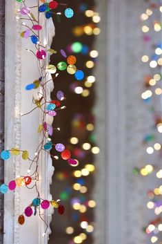 colorful lights are hanging from the side of a window in front of a wall with white curtains